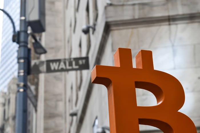 A Bitcoin symbol next to a street name sign saying Wall Street.