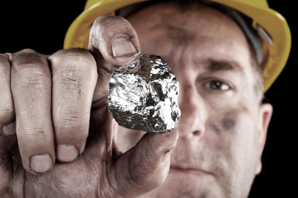 A person with a mining helmet on holding a silver nugget.