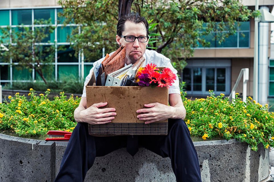 Photo of an out-of-work businessman, sitting outside his office building with his box of meager belongings as he gets rained on.  