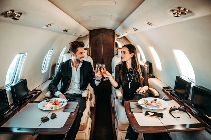 Two people on a private jet are holding wine glasses.