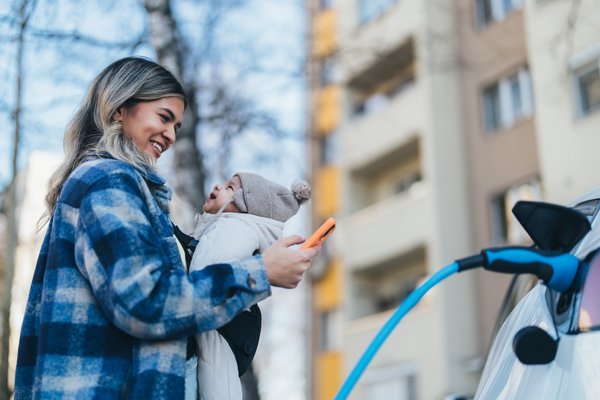 A parent holds an infant while charging an electric vehicle