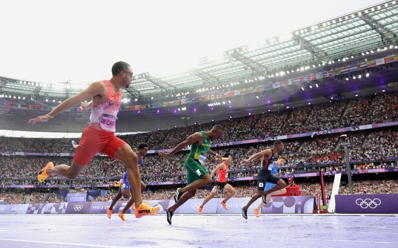 Male sprinters are seen crossing the finish line in a track and field event.