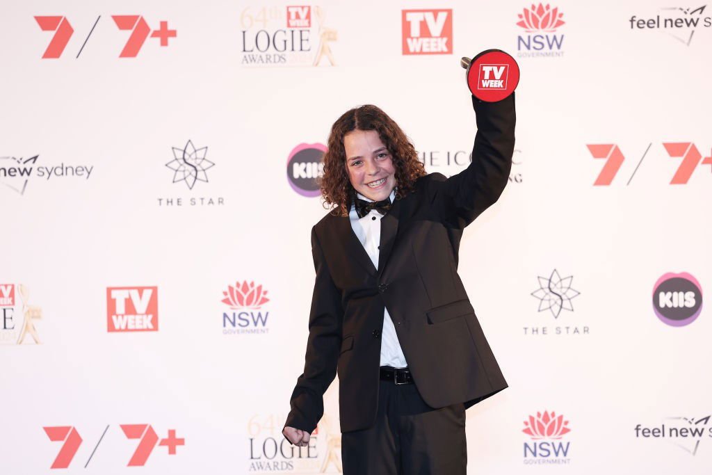 Felix Cameron, a 15-year-old boy with long hair, smiles brightly as he holds up a Logie.