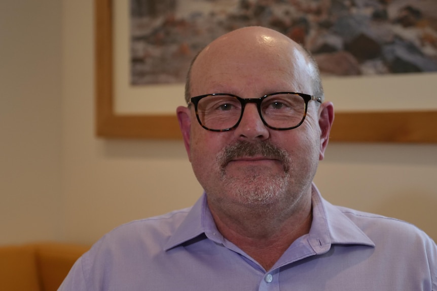 A man sits in an office and smiles at the camera