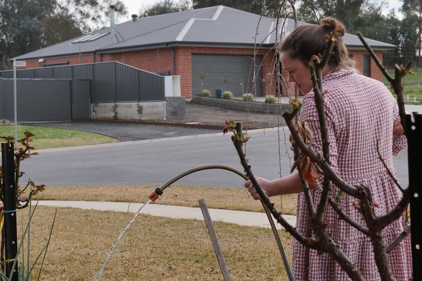 A woman waters her garden but the water stream is low