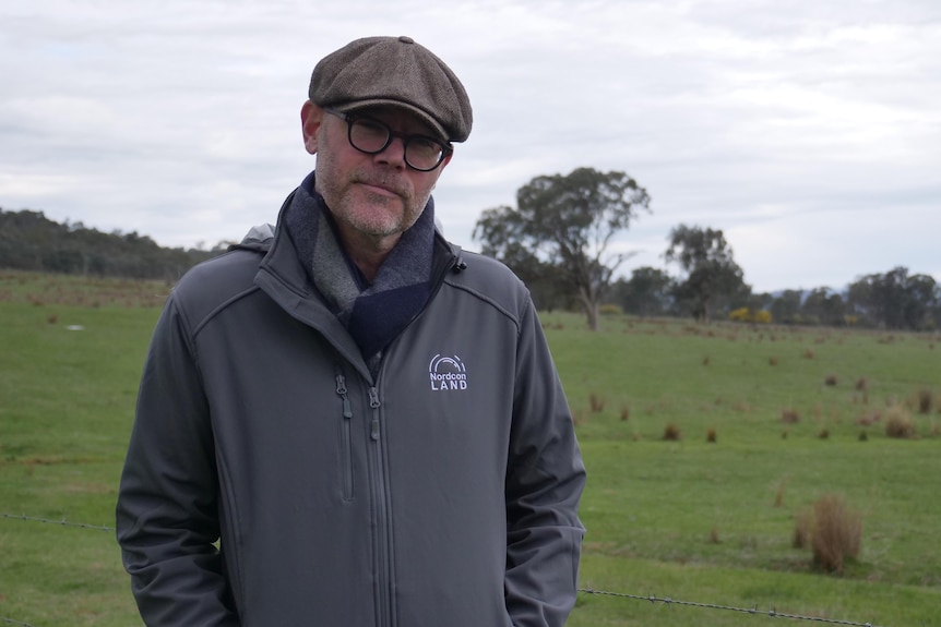 A man stands next to an empty paddock.