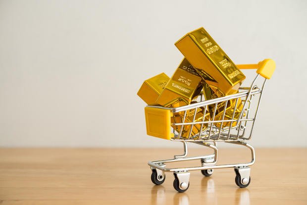 Gold bars in shopping trolley on wooden table with white wall background copy space. 